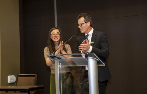 Ying-Ling Esfandi and Michael Bendetti applauding while standing at a podium