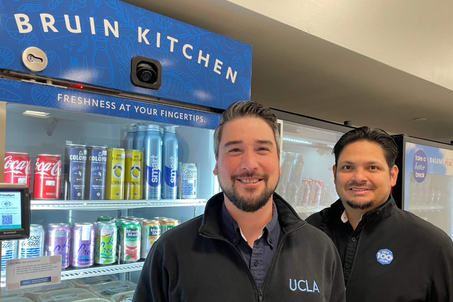 Two men in front of the grab and go at Bruin Kitchen
