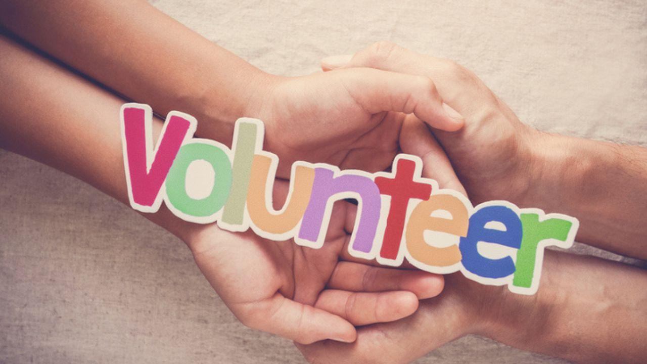 Two people's hands cradling a colorful "volunteer" sign.