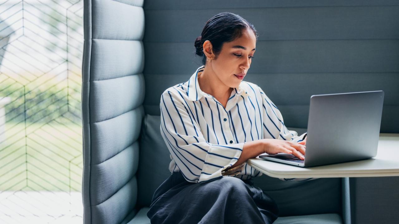 A concentrated woman diligently using a laptop in a private, modern office workspace.