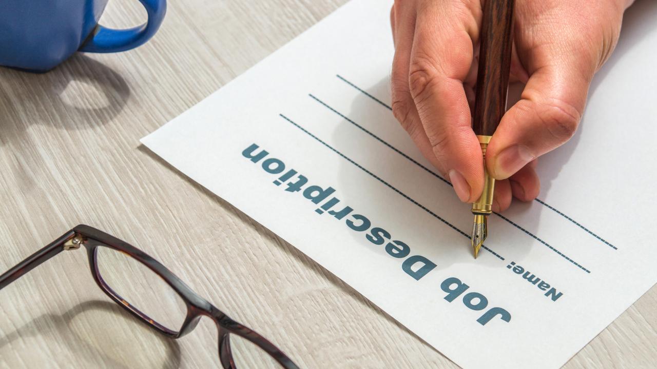 Person's hand holding a pen writing on a job description form