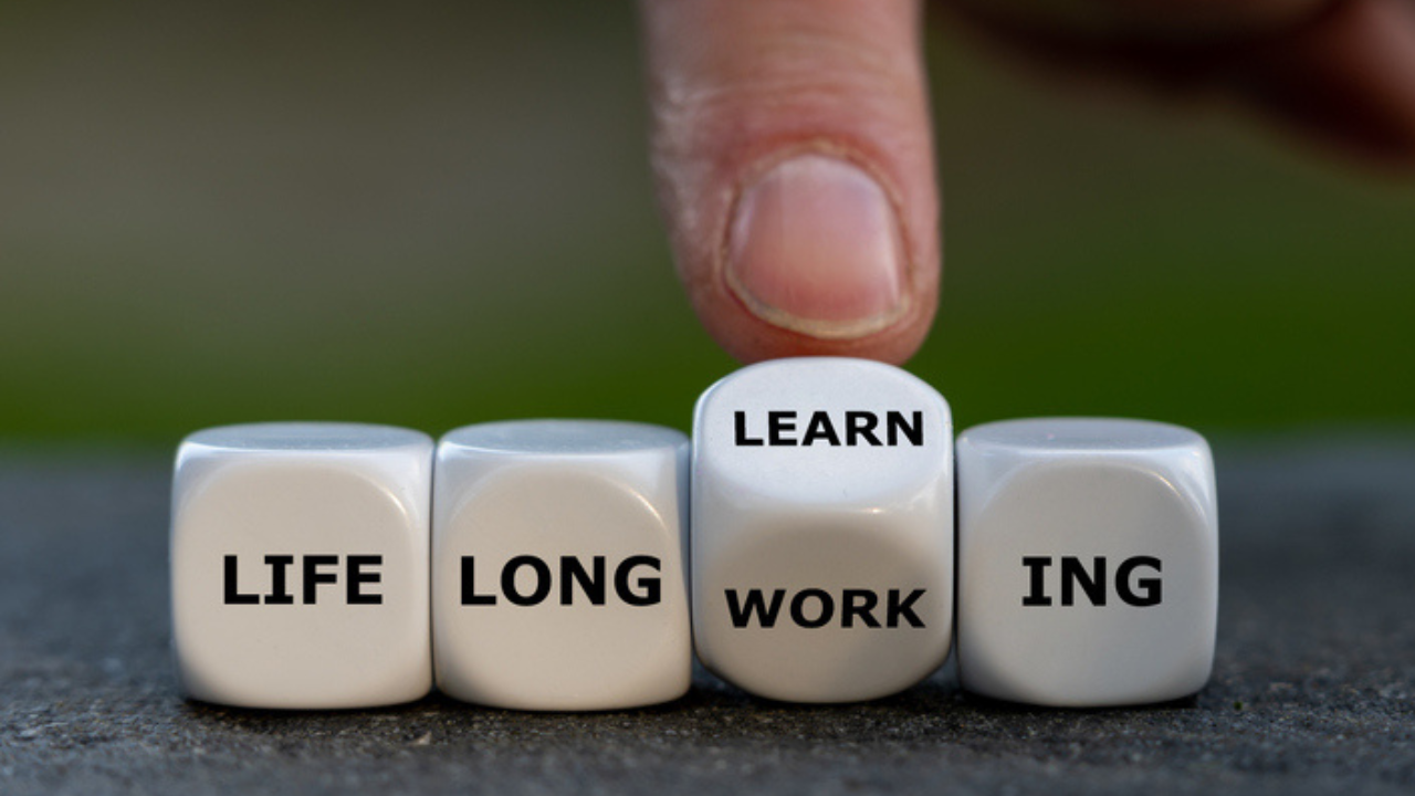 A finger on a dice about to flip Life Long Work-ing to Life Long Learn-ing