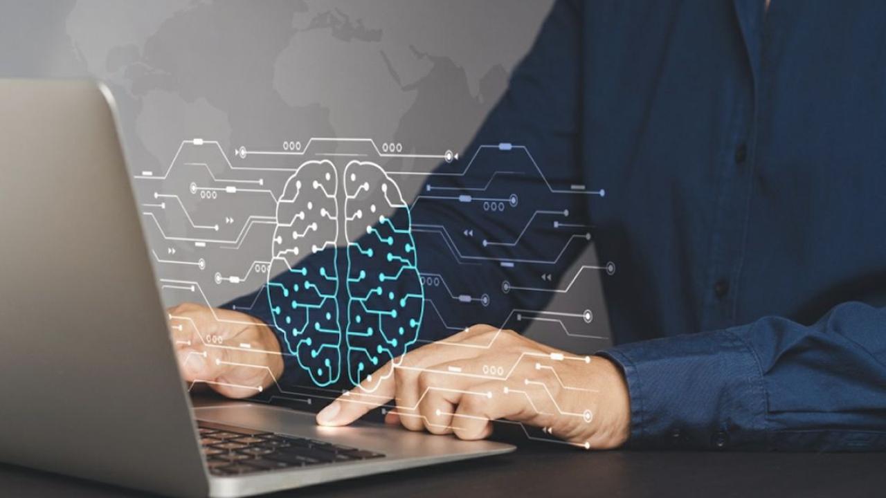 Photo of person using laptop (showing hands and chest), with a graphic of a brain overlaid