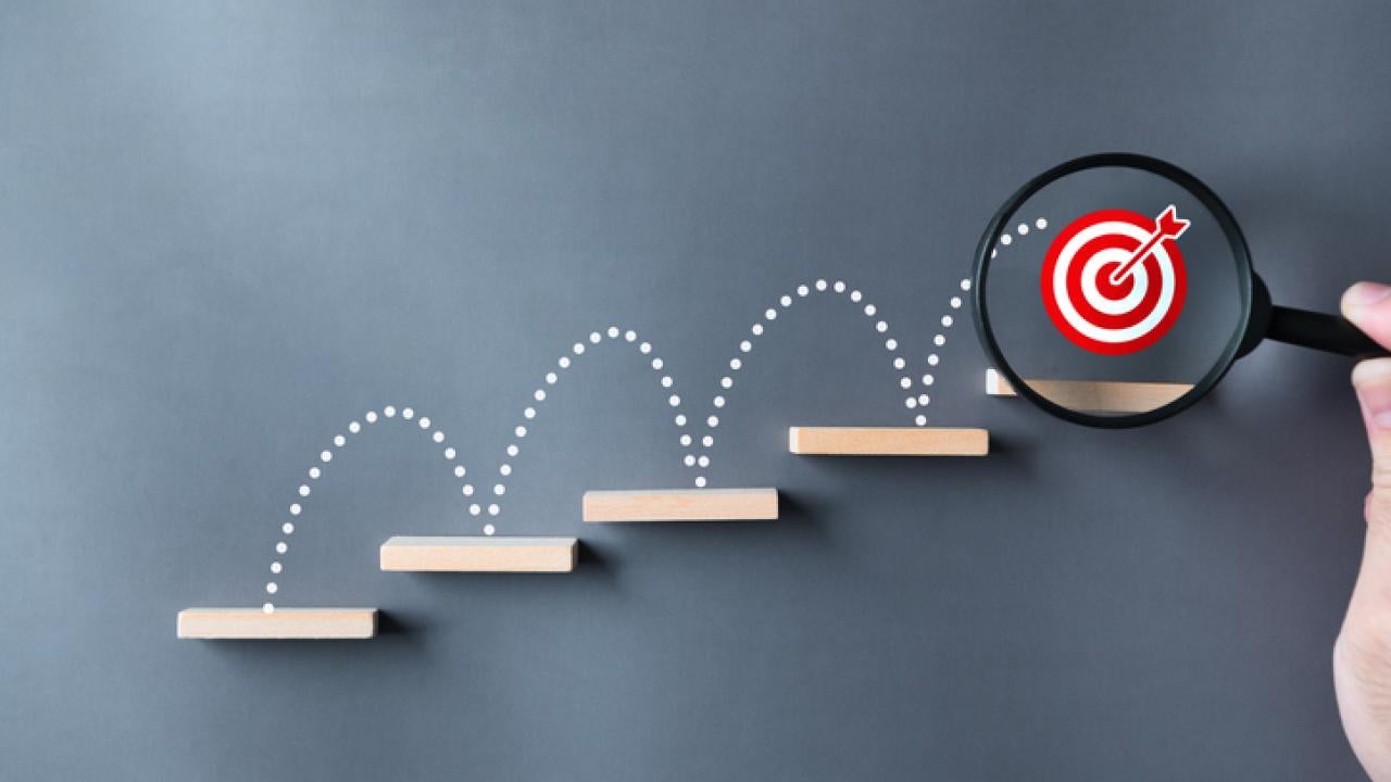 Leaping lines up a staircase with a bullseye under a magnifying glass on the last step