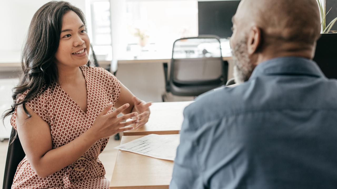 Male and female employees having a conversation while sitting across from one another at a desk