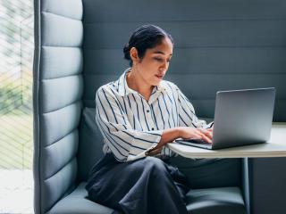 A concentrated woman diligently using a laptop in a private, modern office workspace.