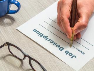 Person's hand holding a pen writing on a job description form
