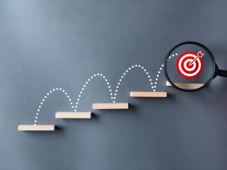 Leaping lines up a staircase with a bullseye under a magnifying glass on the last step