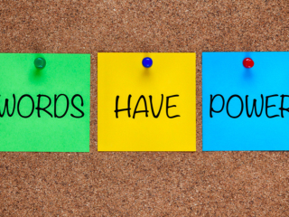 A group of colorful notes pinned to a cork board which spell Words Have Power.